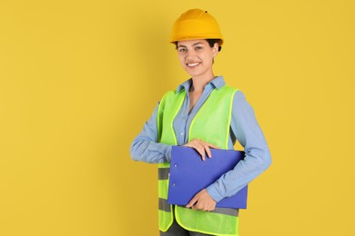 Photo of Engineer in hard hat with clipboard on yellow background, space for text