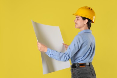 Engineer in hard hat with draft on yellow background, space for text