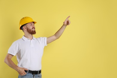 Engineer in hard hat pointing at something on yellow background, space for text