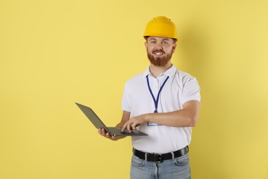 Engineer in hard hat with laptop on yellow background, space for text