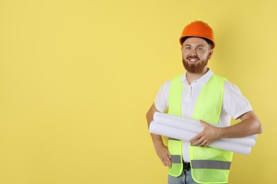 Photo of Engineer in hard hat with drafts on yellow background, space for text