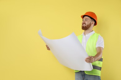 Engineer in hard hat with draft on yellow background, space for text