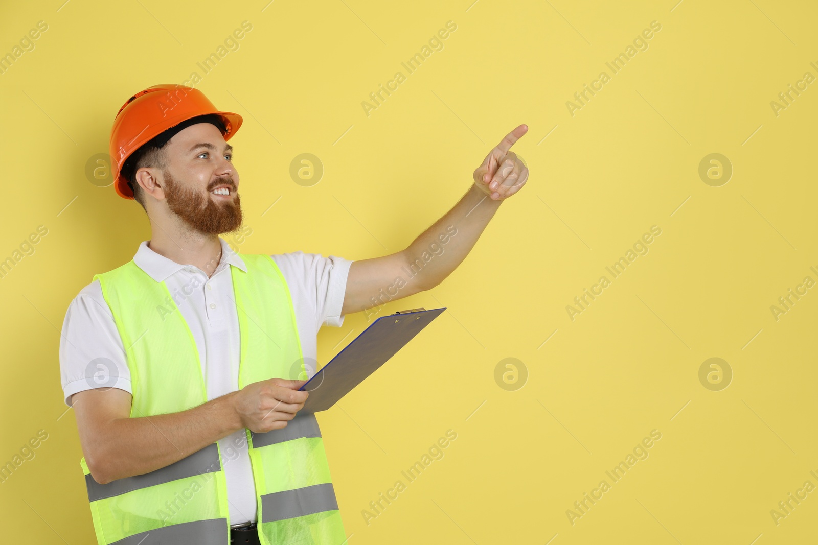 Photo of Engineer in hard hat with clipboard on yellow background, space for text