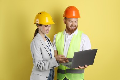 Engineers in hard hats with laptop on yellow background