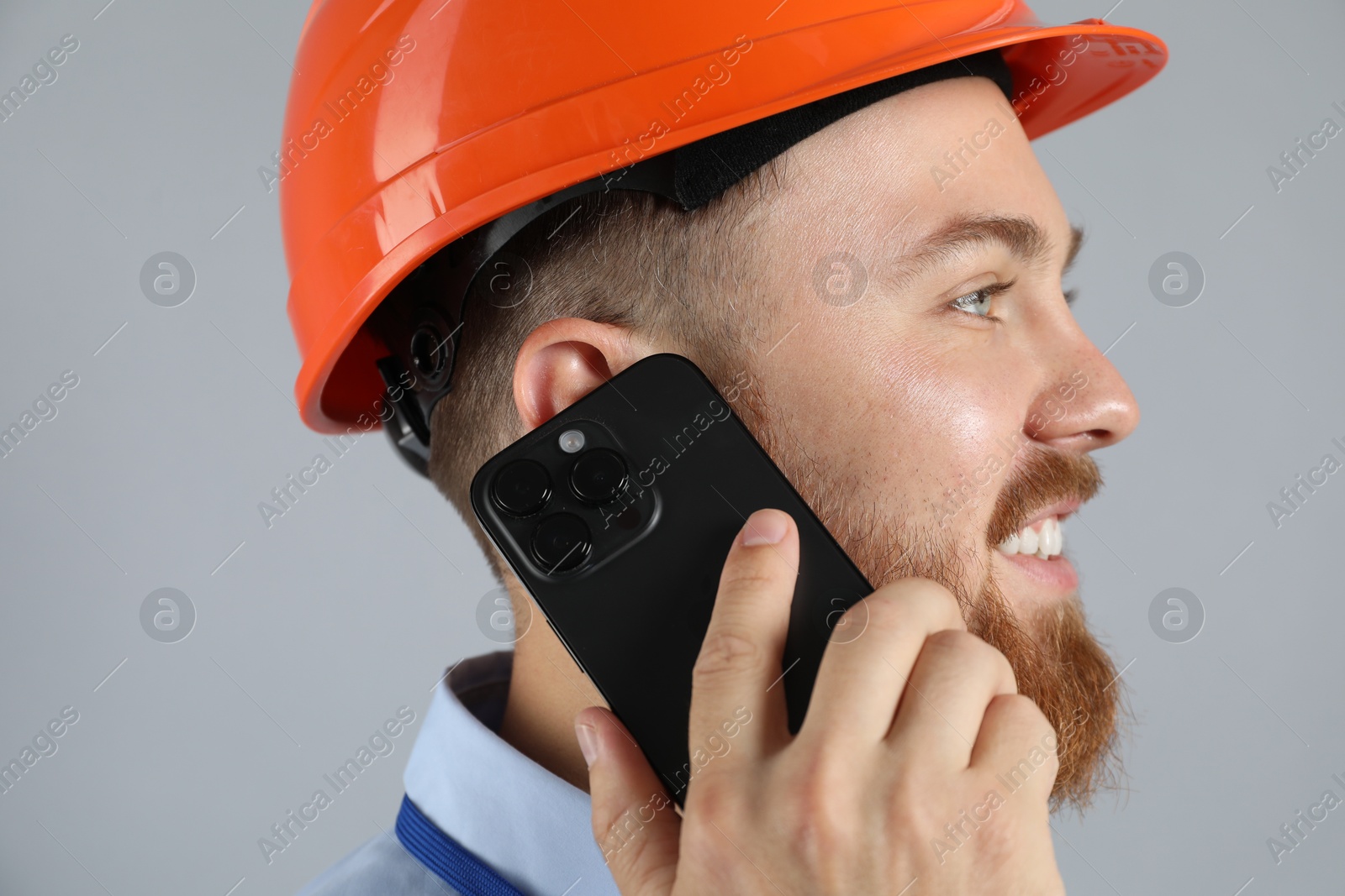 Photo of Engineer in hard hat talking on smartphone against grey background