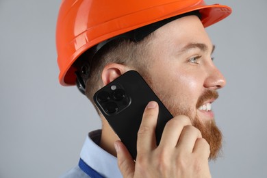 Photo of Engineer in hard hat talking on smartphone against grey background