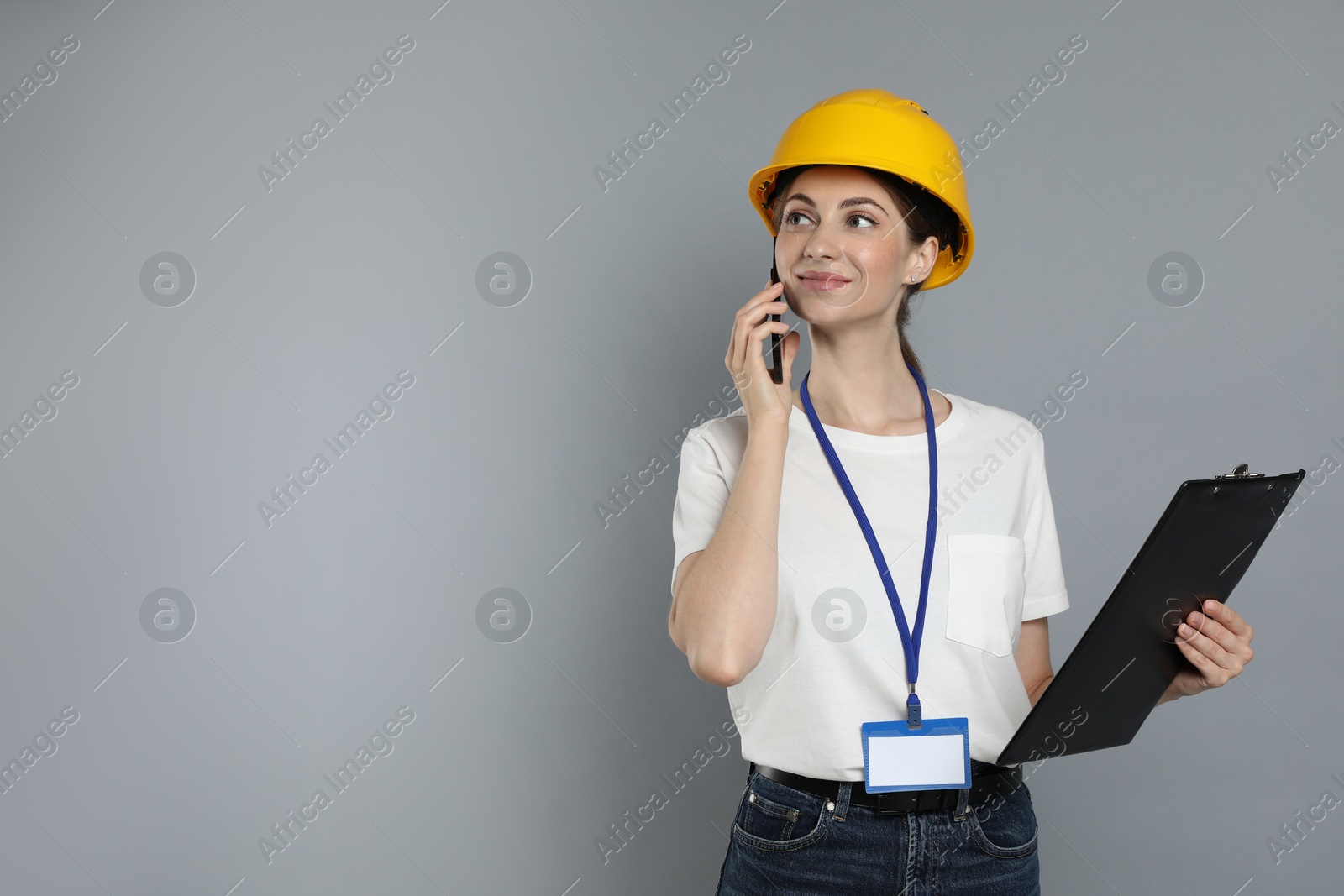 Photo of Engineer in hard hat with clipboard talking on smartphone against grey background, space for text