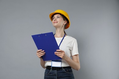 Photo of Engineer in hard hat with clipboard on grey background, low angle view