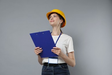 Engineer in hard hat with clipboard on grey background, low angle view