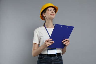 Photo of Engineer in hard hat with clipboard on grey background, low angle view