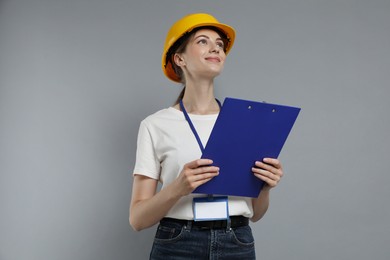 Engineer in hard hat with clipboard on grey background, low angle view