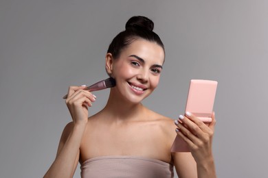 Photo of Smiling woman with cosmetic product applying makeup on light grey background