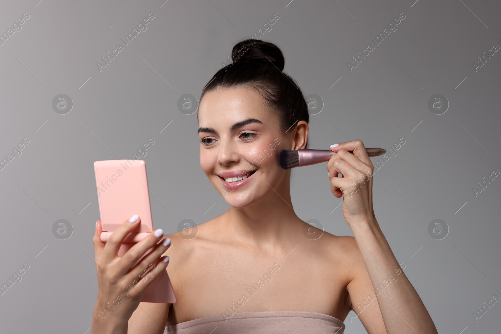 Photo of Smiling woman with cosmetic product applying makeup on light grey background