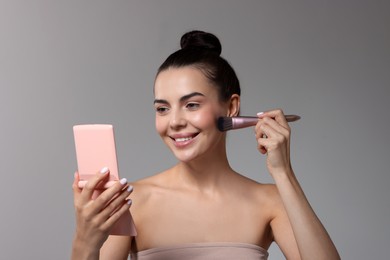 Smiling woman with cosmetic product applying makeup on light grey background