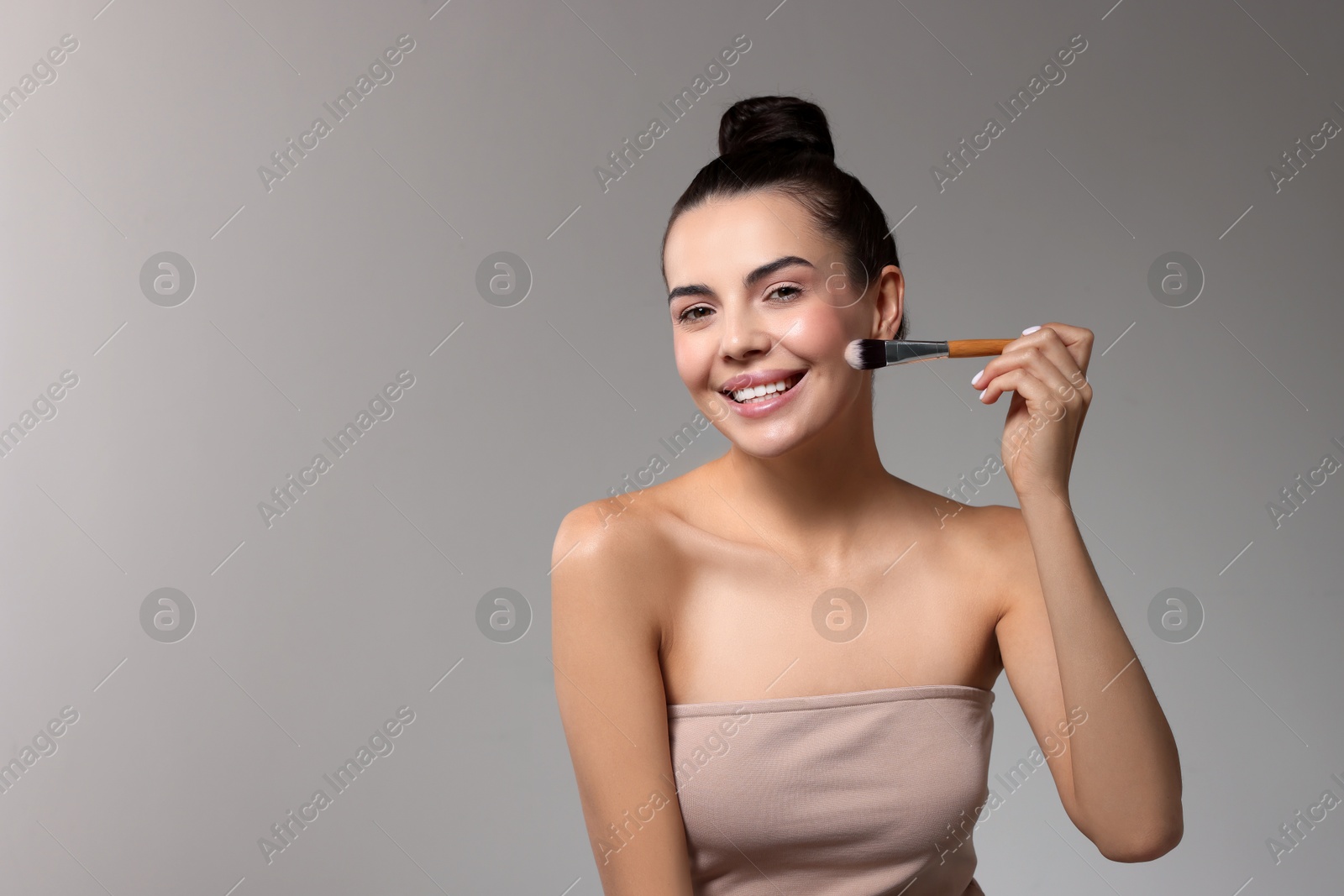 Photo of Smiling woman applying makeup with brush on light grey background. Space for text