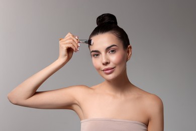 Photo of Beautiful woman applying makeup with brush on grey background