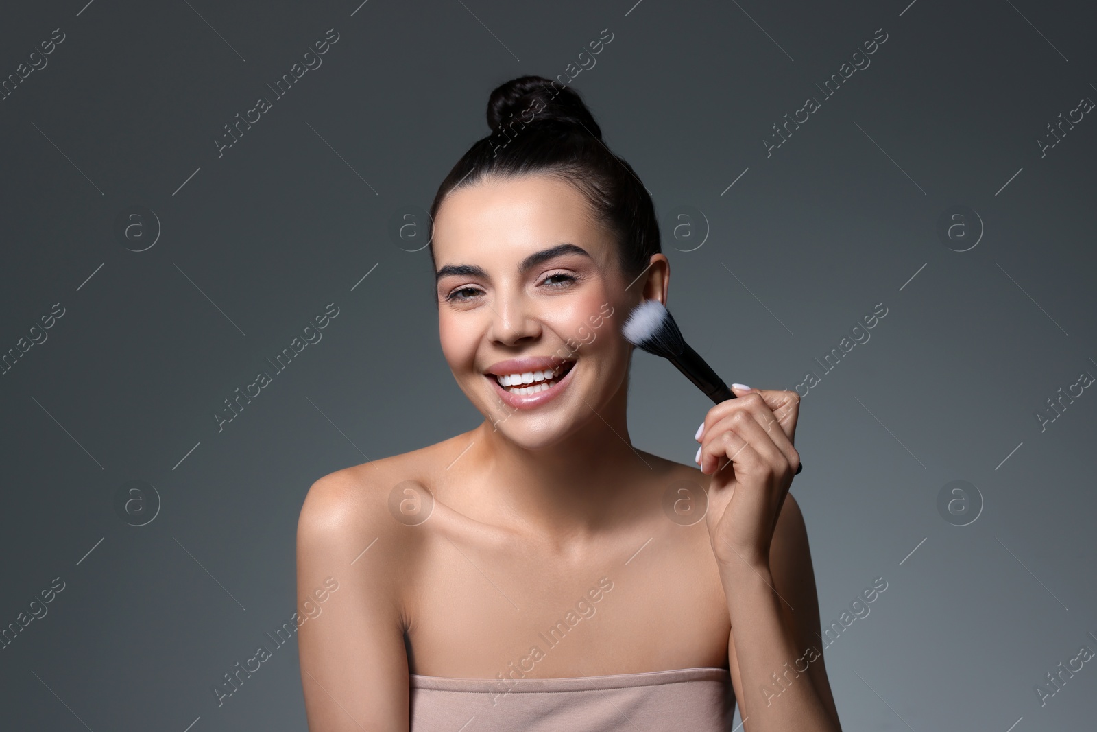 Photo of Smiling woman with makeup brush on grey background