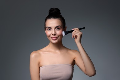 Photo of Beautiful woman applying makeup with brush on grey background