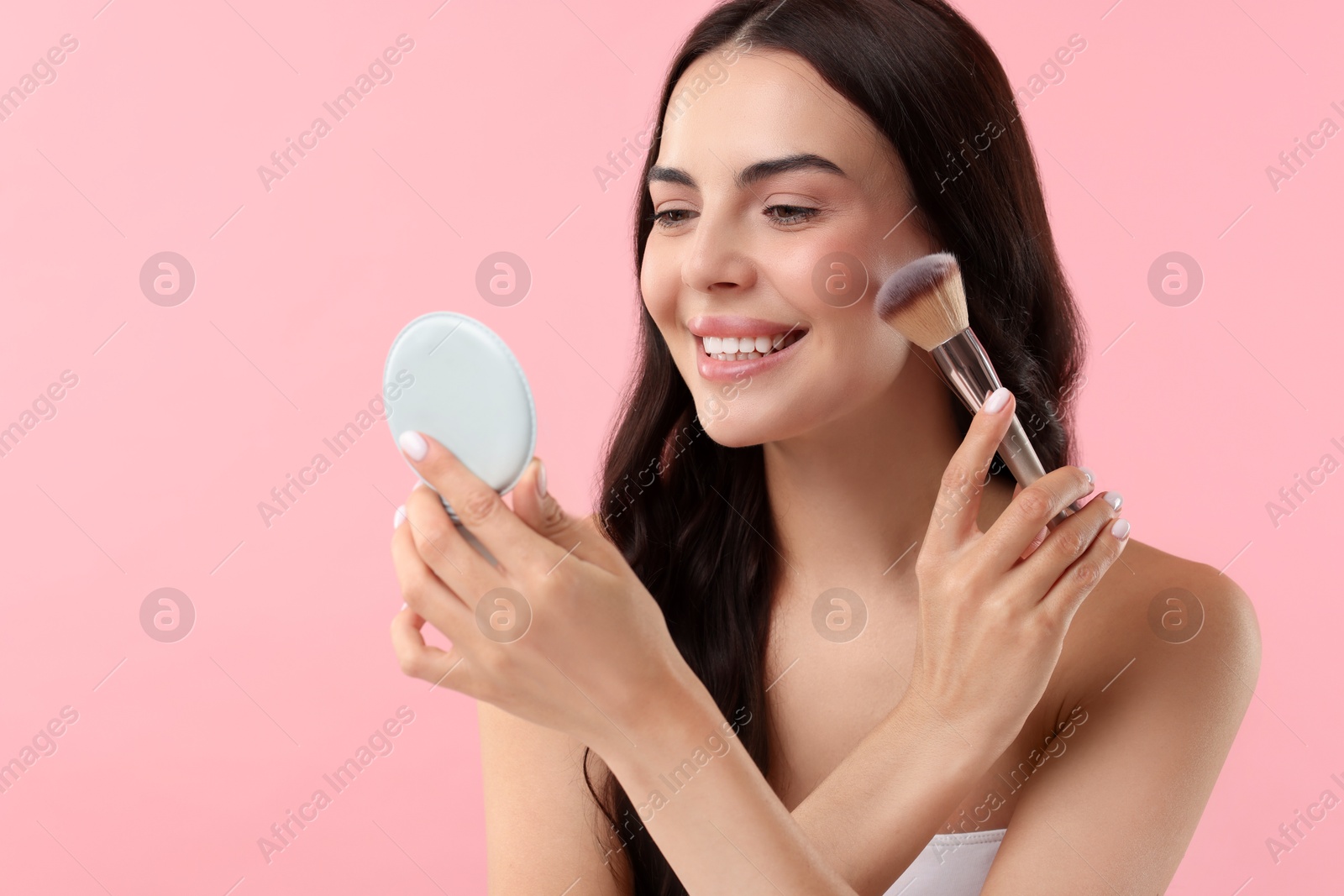 Photo of Beautiful makeup. Smiling woman applying blush with brush on pink background