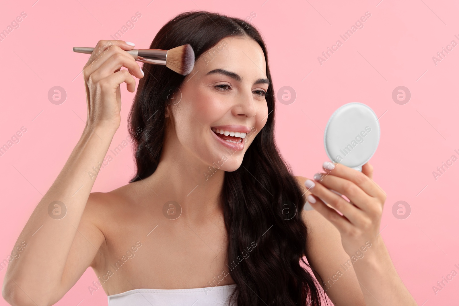 Photo of Smiling woman with cosmetic product applying makeup on pink background