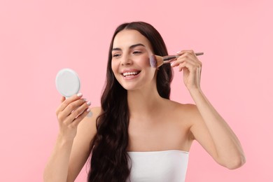 Photo of Smiling woman with cosmetic product applying makeup on pink background