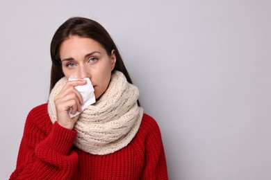 Sick woman with tissue on grey background, space for text. Cold symptoms