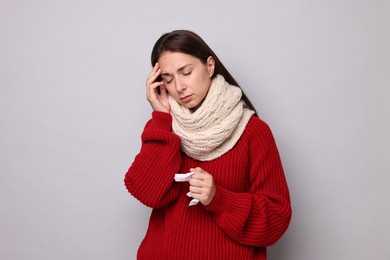 Sick woman with tissue on grey background. Cold symptoms