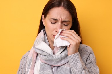 Sick woman with tissue on orange background. Cold symptoms