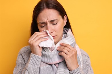 Sick woman with tissue on orange background. Cold symptoms