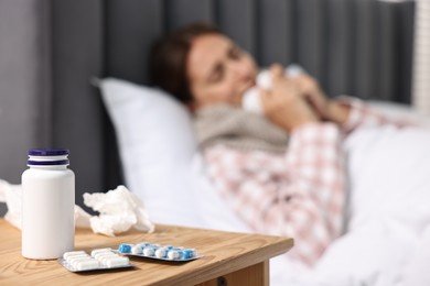 Photo of Sick woman with tissue in bed, focus on different pills on wooden bedside. Cold symptoms