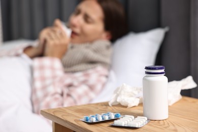 Sick woman with tissue in bed, focus on different pills on wooden bedside. Cold symptoms