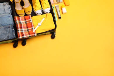 Open suitcase with traveler's belongings on yellow background, flat lay. Space for text