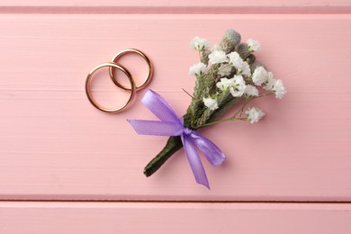 Small stylish boutonniere and rings on pink wooden table, flat lay