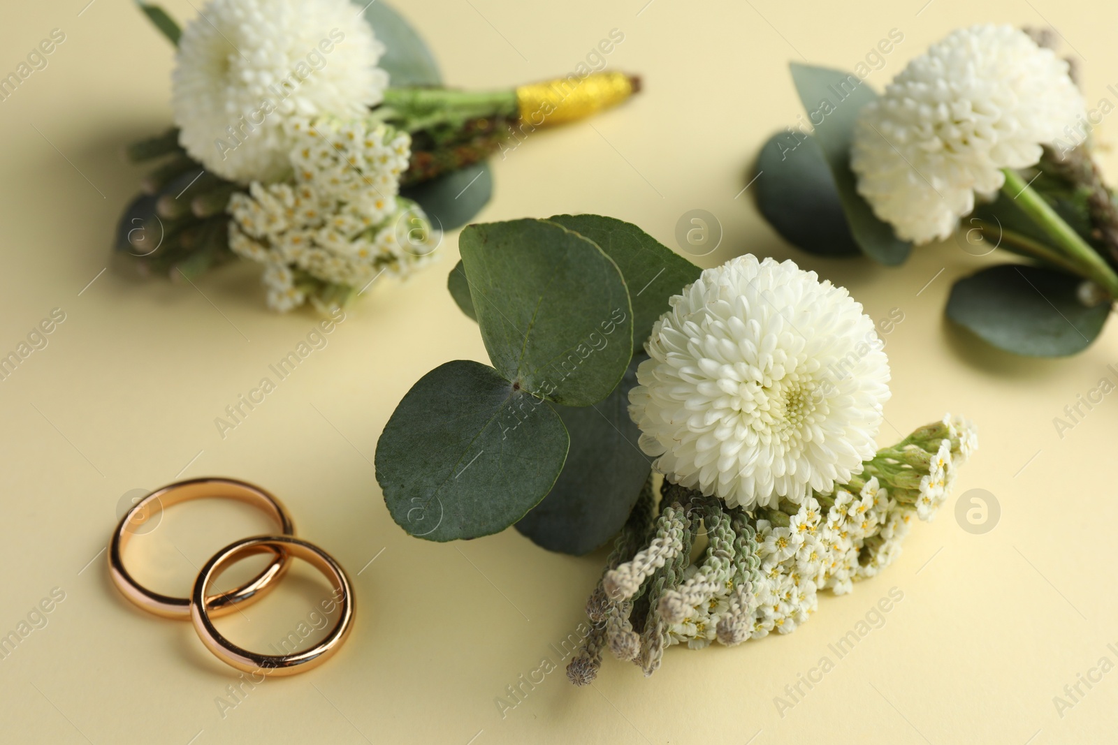 Photo of Small stylish boutonnieres and rings on beige background, closeup