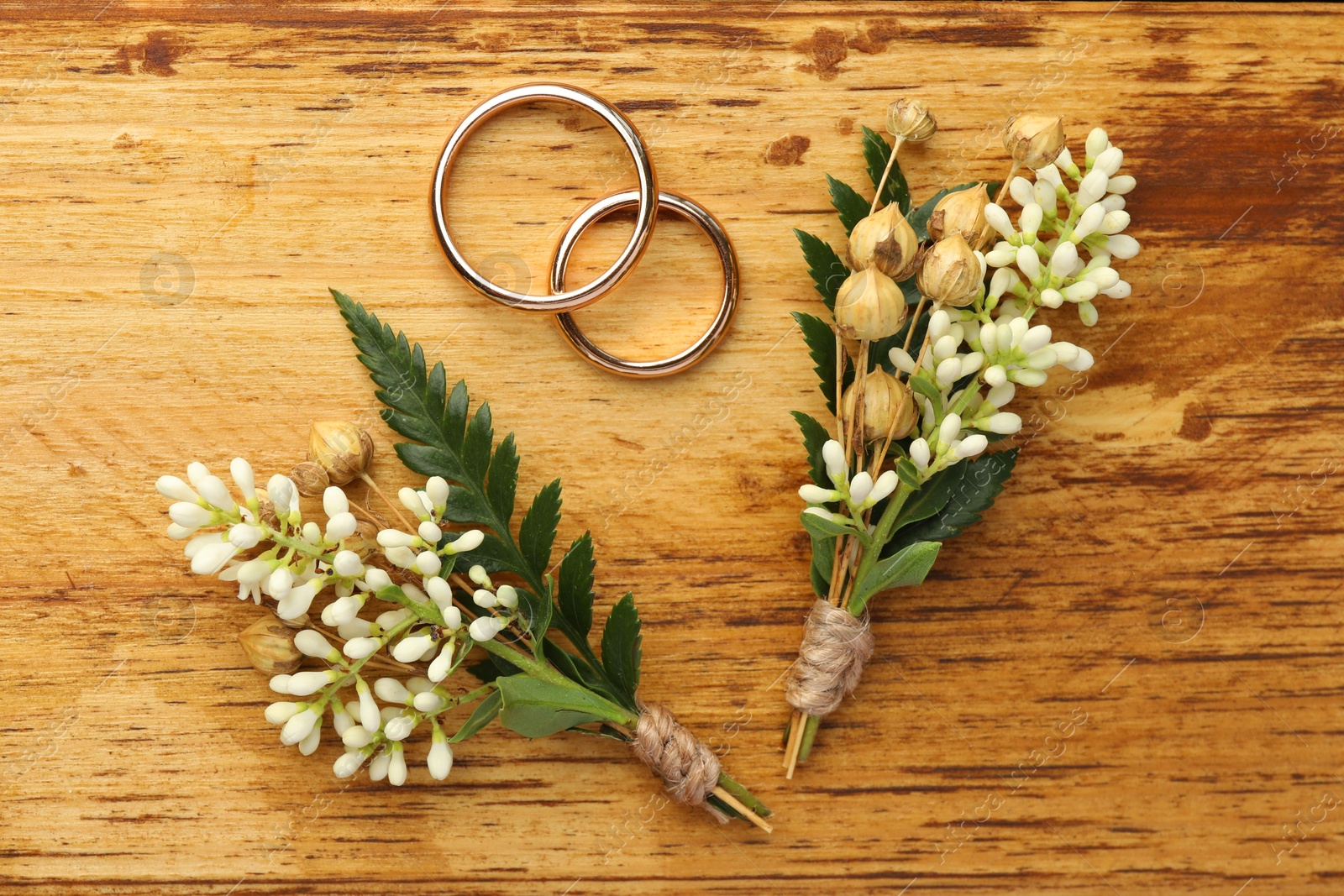 Photo of Small stylish boutonnieres and rings on wooden table, flat lay