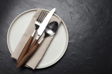 Photo of Stylish cutlery, plate and napkin on black table, top view. Space for text