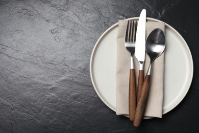 Photo of Stylish cutlery, plate and napkin on black table, top view. Space for text