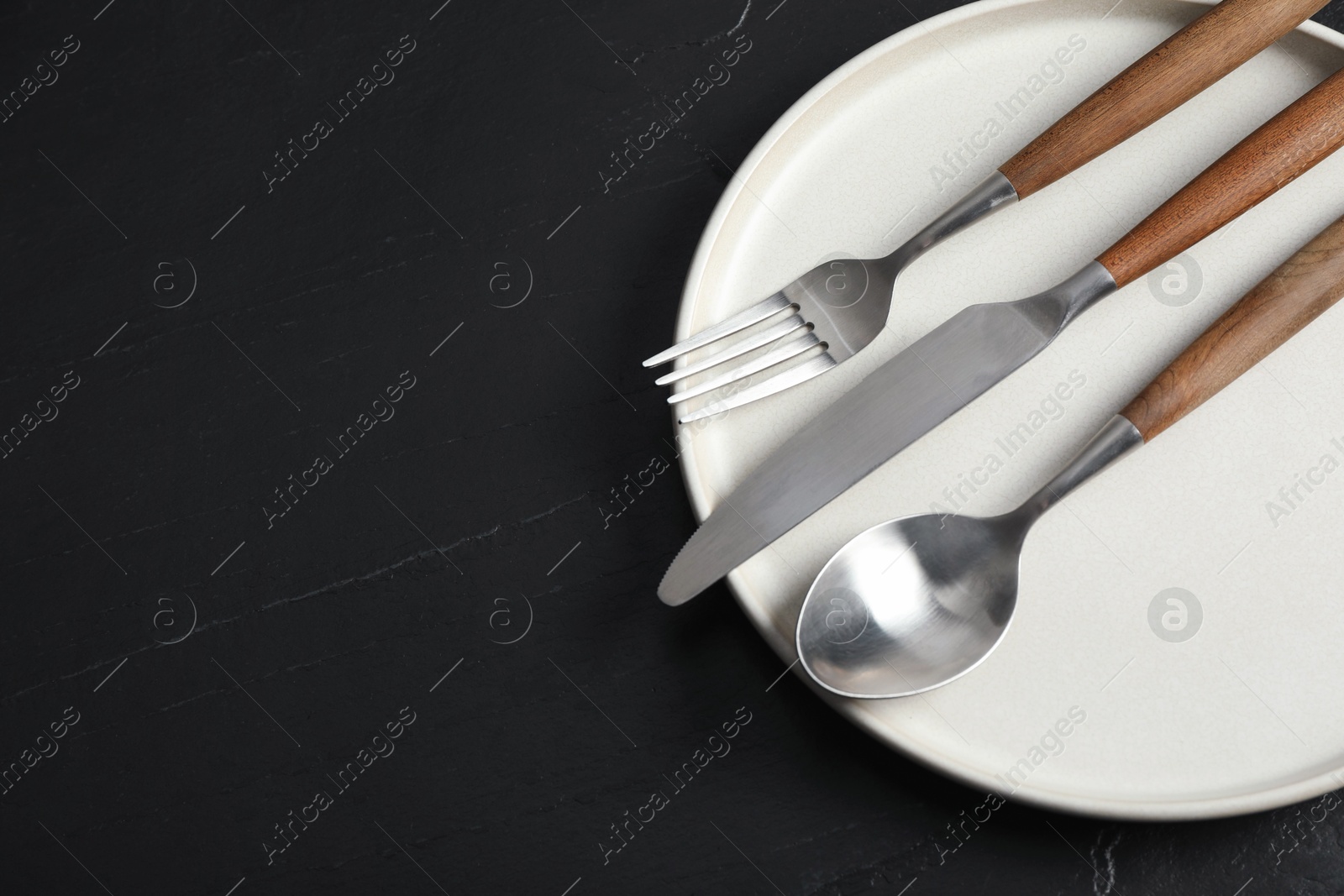 Photo of Stylish cutlery and plate on black table, top view. Space for text