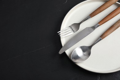 Stylish cutlery and plate on black table, top view. Space for text