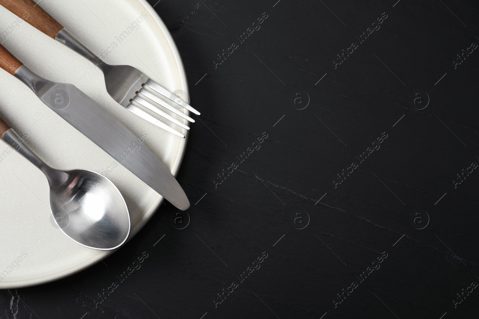 Photo of Stylish cutlery and plate on black table, top view. Space for text