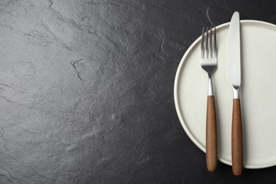 Photo of Stylish cutlery and plate on black table, top view. Space for text