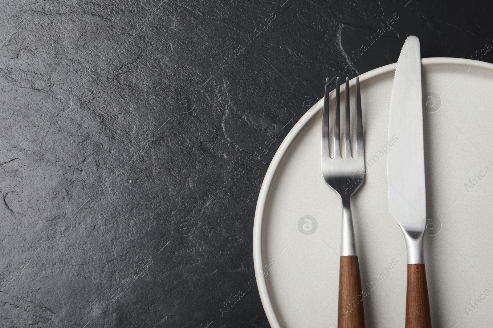 Photo of Stylish cutlery and plate on black table, top view. Space for text