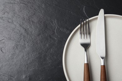 Photo of Stylish cutlery and plate on black table, top view. Space for text