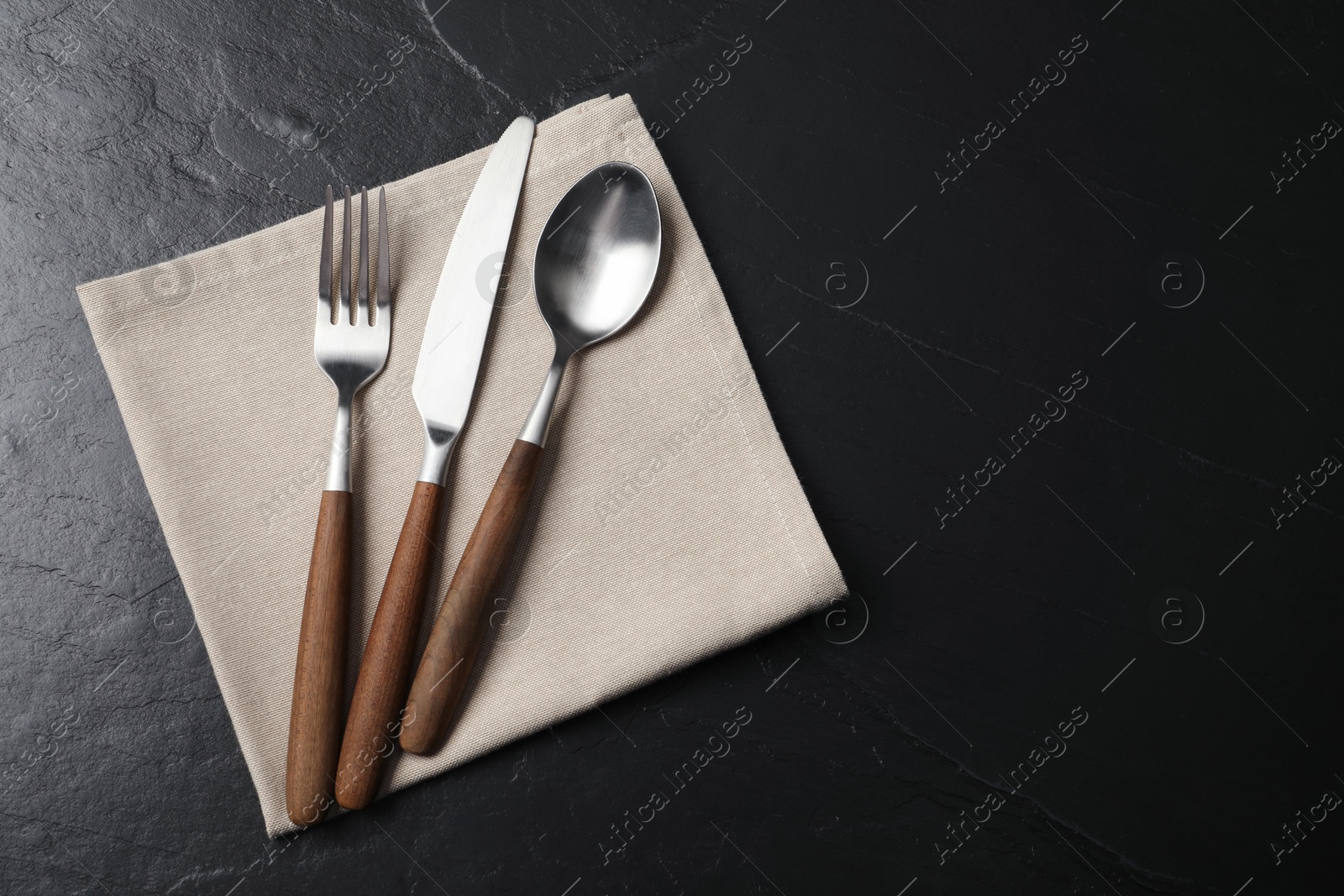 Photo of Stylish cutlery and napkin on black table, top view. Space for text