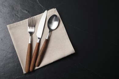 Photo of Stylish cutlery and napkin on black table, top view. Space for text