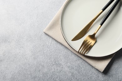 Photo of Stylish golden cutlery, plate and napkin on grey table, top view. Space for text