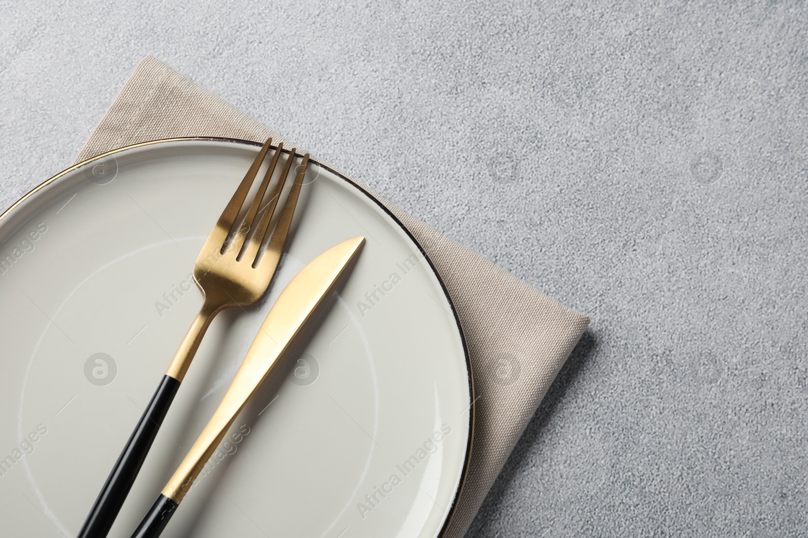 Photo of Stylish golden cutlery, plate and napkin on grey table, top view. Space for text