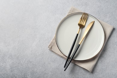 Photo of Stylish golden cutlery, plate and napkin on grey table, top view. Space for text