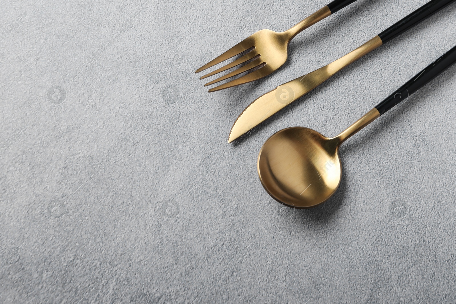 Photo of Stylish golden cutlery on grey table, above view. Space for text