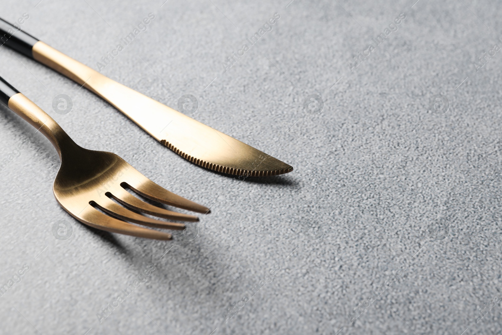 Photo of Stylish golden cutlery on grey table, closeup. Space for text